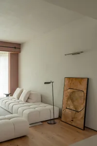 A minimalist living room featuring a cream-colored floor lamp, a white couch with tufted cushions, and an abstract painting i