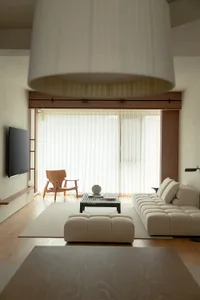 A minimalist living room with neutral-toned fabric furniture, wood accents, and large windows.