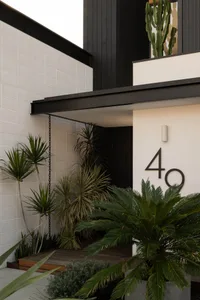Modern front door entryway featuring concrete, wood, and lush green plants