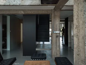 A modern industrial living space with concrete columns, black staircase, and black leather furniture.