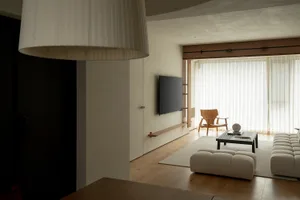 A modern, minimalist living room with a white rug, a white sofa, and a wooden coffee table in front of a large window with wh