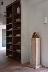 A modern interior design featuring a tall wooden shelf with contemporary art and crafts, set against wooden flooring.