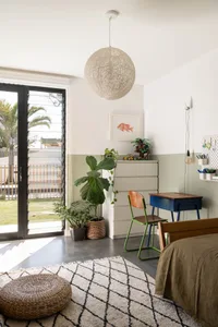 A modern minimalist bedroom featuring concrete flooring, a woven rug, and a green plant.