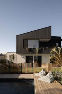 Modern beach house with wooden deck and glass fence surrounding a concrete pool.