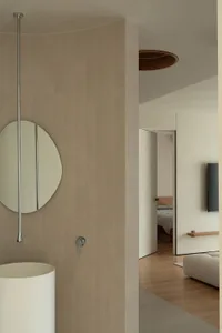 A minimalist bathroom with a tile wall and floor, featuring an oval mirror and a modern pedestal sink.