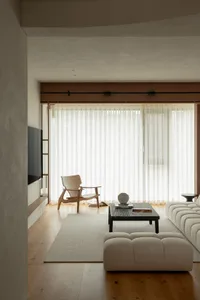 Modern minimalist living room with natural wood floor, white fabric sofa, glass coffee table, and white sheer curtains.