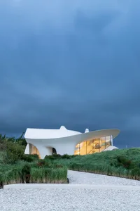 Modern white building with curved facade and large windows at dusk
