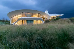 Modern residential house with white, curved glass facade and interior lights on.