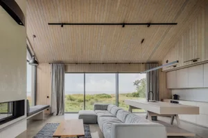 A modern minimalist living room with wooden walls and a view of the ocean, featuring a gray sectional sofa and a wooden coffe
