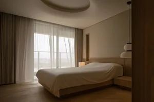 Modern bedroom with a neutral color palette, featuring a bed with a wooden frame and a large window with curtains.