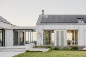 Modern residential building with rear yard featuring concrete deck and steps, solar panels on the roof, and green grass.