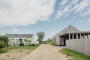 Modern house exterior with concrete and wooden textures, set against a blue sky with clouds.