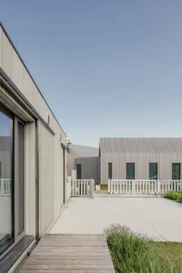 Modern residential exterior with wooden board and batten siding and a white picket fence.