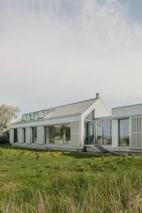 A modern residential house with glass walls and a metal-clad exterior.