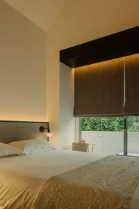 A minimalist bedroom with white walls, a textured fabric bedspread, and a window with dark blinds.