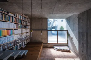A minimalist library with concrete walls and a large bookshelf filled with books.