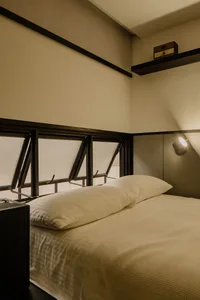 A minimalist bedroom with a bed, white bedding, a metal headboard, and large windows.