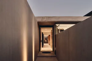 A modern interior space featuring a concrete pathway leading to a warmly lit room.