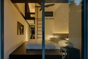 A modern minimalist bedroom with a wooden bed platform and white bedding, illuminated by soft lighting.