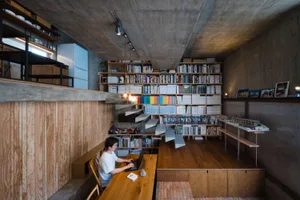 A modern minimalist living room with wooden elements, featuring a large bookshelf filled with books and magazines, a concrete