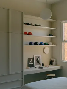 A minimalist bedroom with white shelves displaying various items like shoes, hats, and a poster of sneakers.