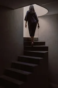 A woman walking up a set of minimalist concrete stairs, viewed from the rear.