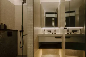 Modern bathroom with tiled walls, minimalist mirror, and metal dimmer switches.