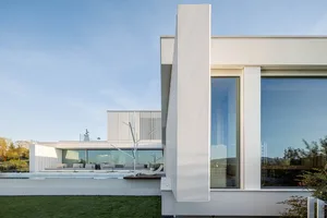A modern house with a white exterior and concrete walls, alongside a pool and green grass.