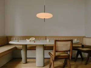 A minimalist dining room featuring a modern, round, concrete table with wooden chairs and a pendant light fixture.