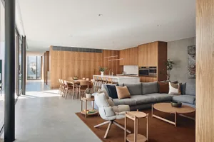 Photograph of a modern indoor wooden living room with a large sofa, coffee tables, and a dining area with a long table and ch