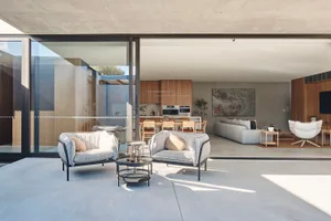 A modern living room featuring a concrete floor and furniture, with a view into the kitchen area.