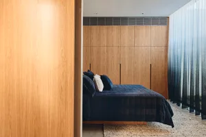 A modern minimalist bedroom with wooden paneling, a navy blue bedspread, and white curtains.