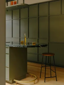 Modern minimalist kitchen with marble countertop and wooden stools, featuring sleek, integrated cabinetry and a high gloss fi
