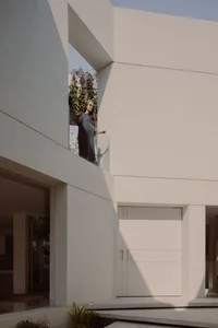 A woman standing on a modern residential entry with concrete elements and a glass window overlooking greenery.