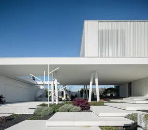 A modern white concrete building with a minimalist design and a spiral staircase leading up to the entrance.