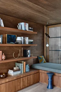 A cozy home office with wooden shelves, a cushioned bench, and a variety of books and decorative items.