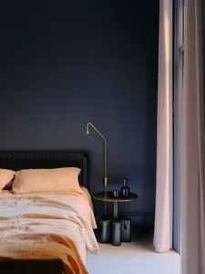A minimalist bedroom with a bed, side table, lamp, and window with curtains.