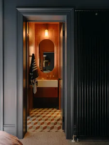 A modern bathroom with orange ceramic tiles, a floating sink, and a round mirror.