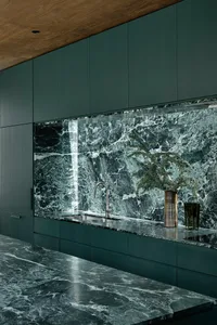 Modern kitchen interior featuring green marble countertops, backsplash, and cabinets.
