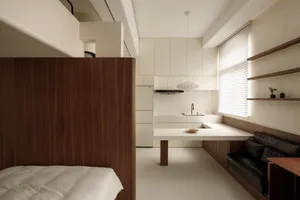 A modern, minimalist kitchen with white laminate countertops and backsplash, featuring a white refrigerator and a small dinin