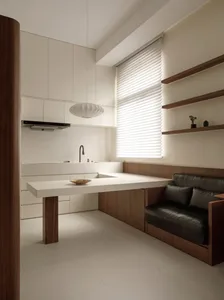 A modern minimalist kitchen with a white marble countertop, white cabinets, and a window with blinds.