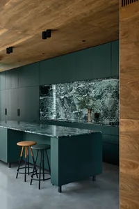 A modern residential kitchen featuring a marble countertop and backsplash against a dark green cabinet backdrop.