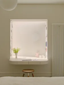 A minimalist office space featuring a white desk area with a laptop, notebook, and vase of flowers, alongside a wooden stool 