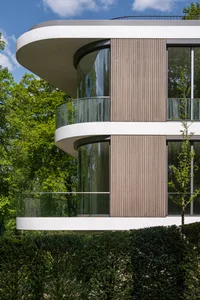 Modern house with glass and wood exterior, featuring curved balconies and greenery.
