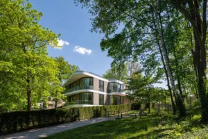 Modern residential house with wooden exterior and glass windows surrounded by greenery on a sunny day.