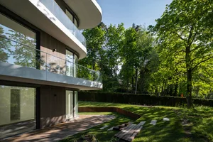Modern house with wood exterior and glass windows surrounded by green trees.