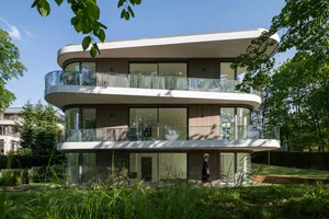 Modern residential building with glass facade and balconies surrounded by greenery.