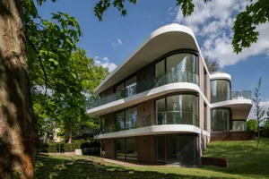 A modern residential building featuring extensive use of glass and wood materials, with a sloped rooftop and large windows.