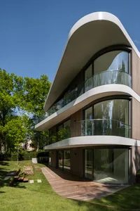 A modern house with a glass extension and curved balcony overlooking a green lawn.