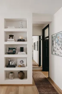 Modern minimalist hallway entrance with built-in shelves featuring decorative vases, books, and a sewing machine.